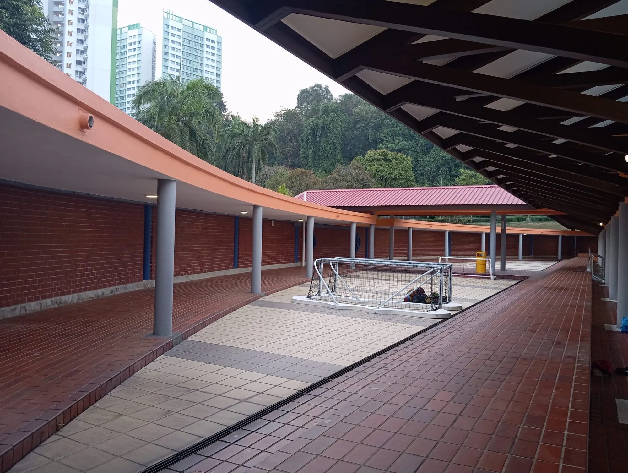 A long covered walkway with red brick walls and a water polo goal stored along it