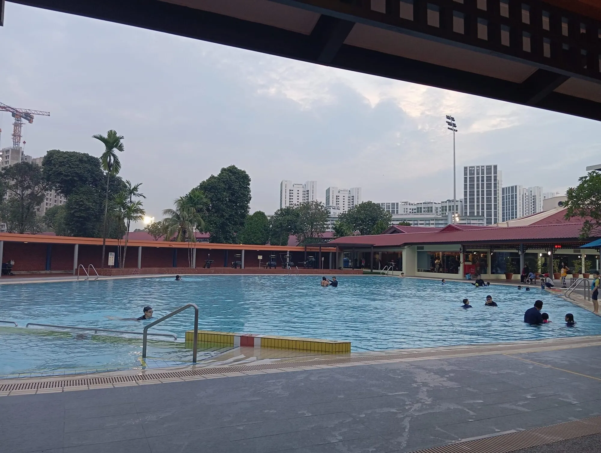 The teaching pool seen from under a covered shelter, with swimmers and a lifeguard chair
