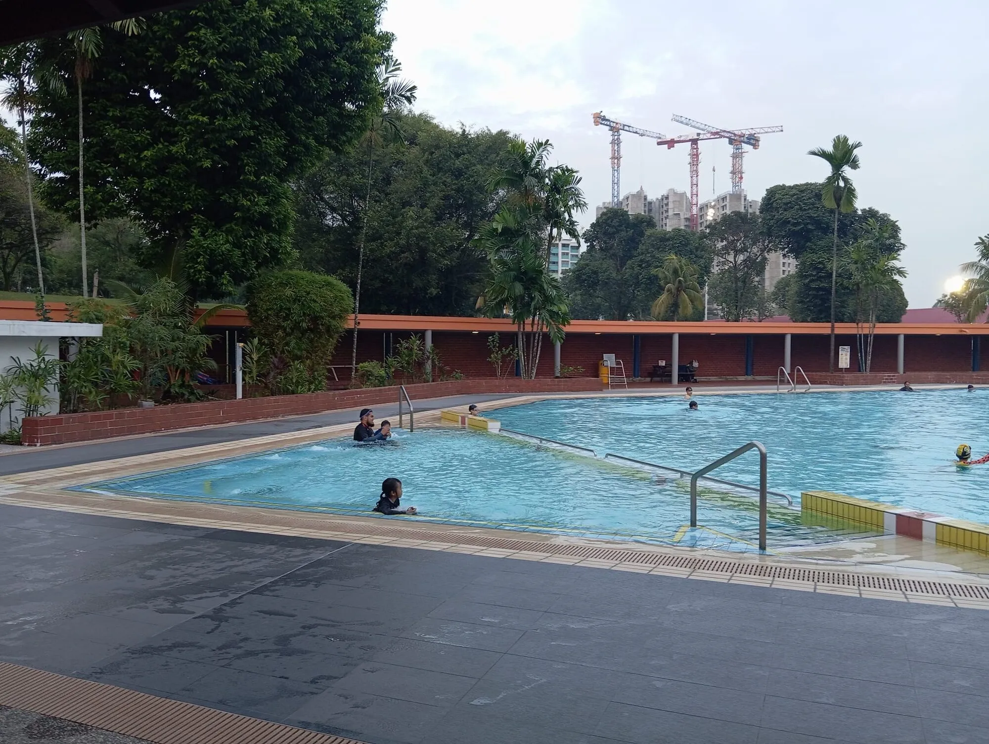 Swimmers in the teaching pool beside a planted garden edge and a brick perimeter wall