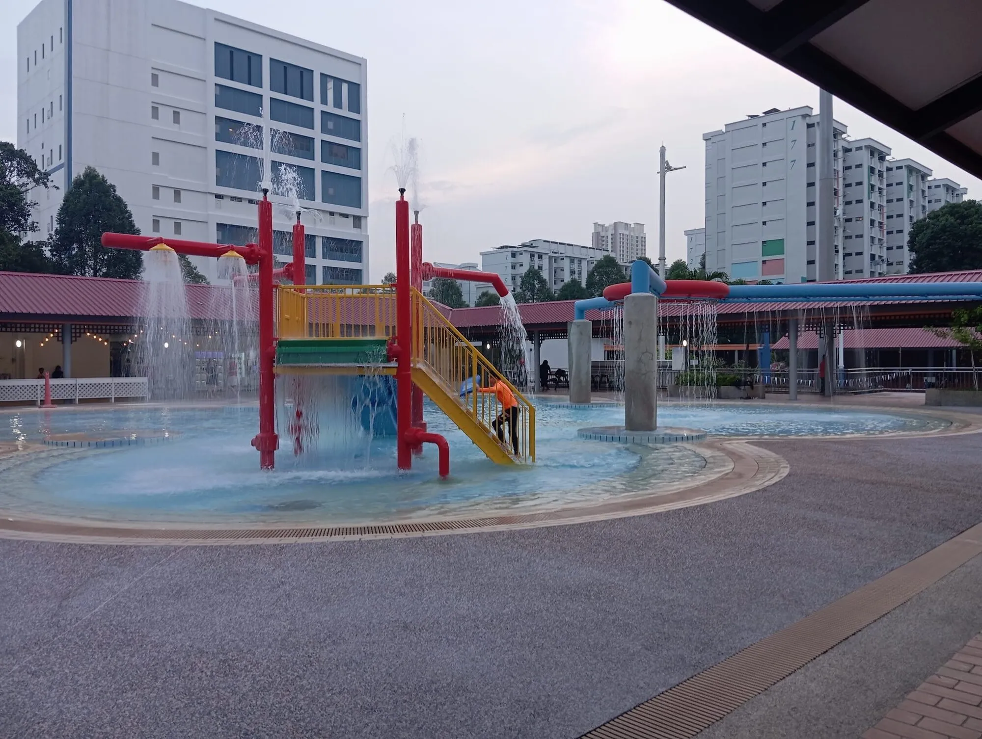 The red and yellow spray tower in the wading pool with water pouring from its buckets